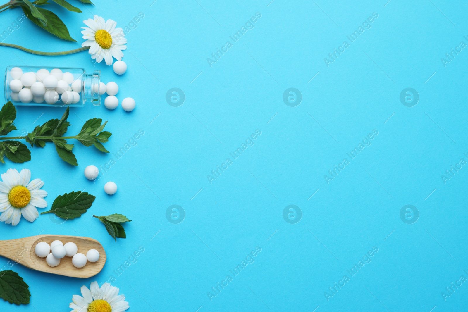 Photo of Homeopathy. Glass bottle, pills, chamomiles and green leaves on light blue background, flat lay. Space for text