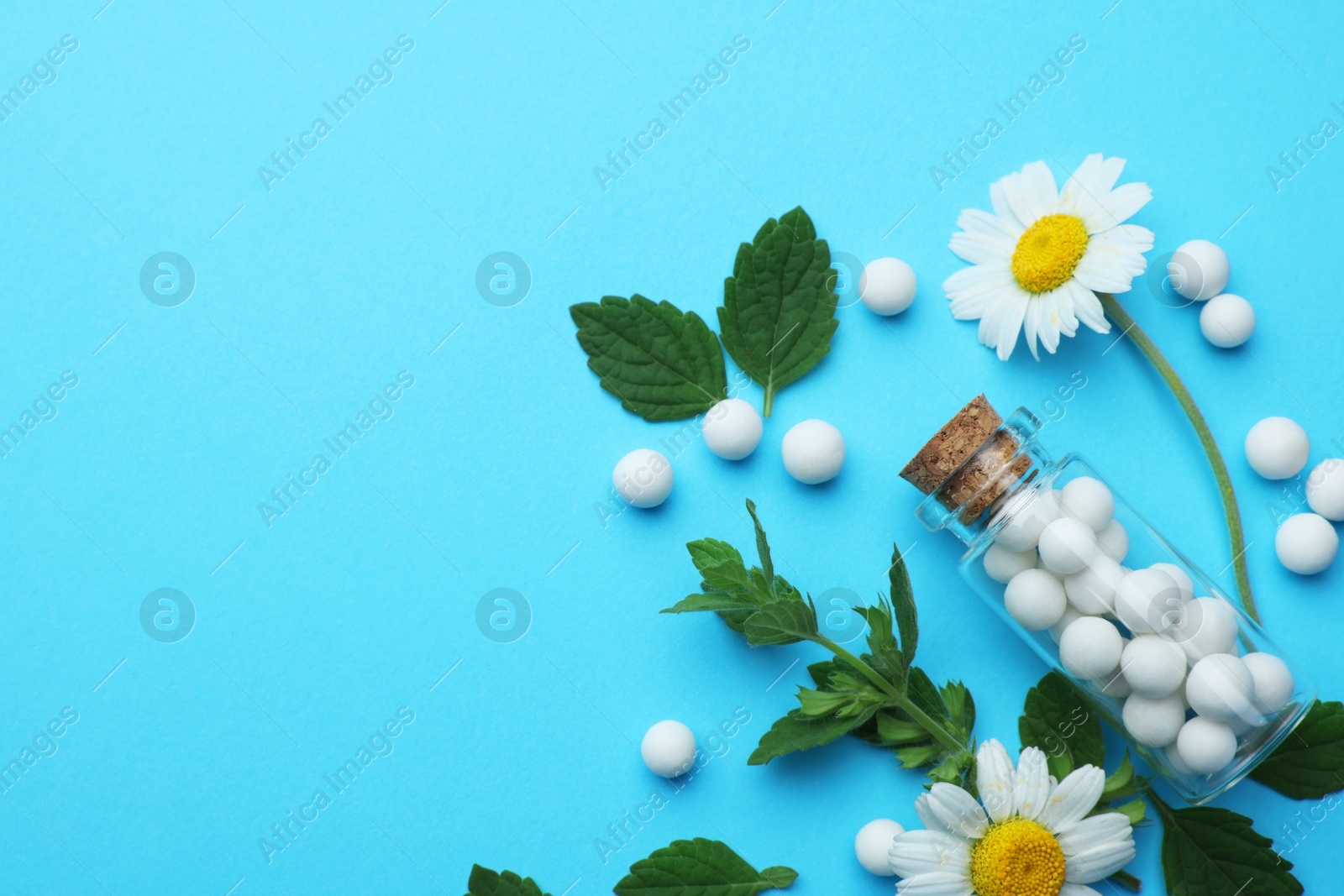 Photo of Homeopathy. Glass bottle, pills, chamomiles and green leaves on light blue background, flat lay. Space for text