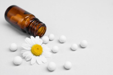 Photo of Homeopathy. Overturned glass bottle, pills and chamomile on white background