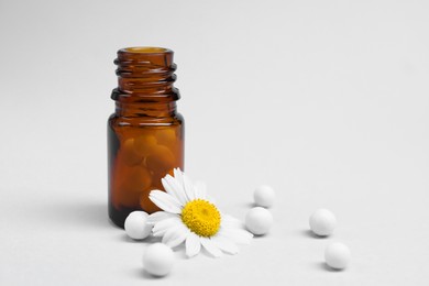 Photo of Homeopathy. Glass bottle, pills and chamomile on white background