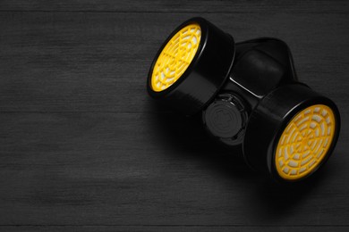 One respirator mask on black wooden background, top view. Space for text