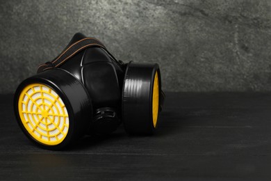 Photo of One respirator mask on black wooden table against gray textured wall, space for text