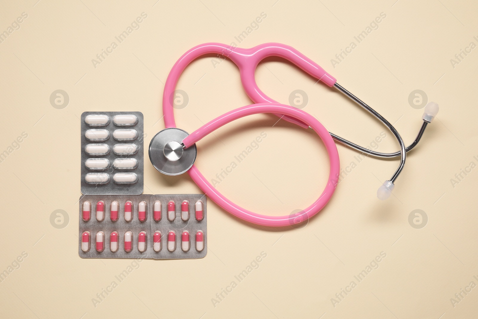 Photo of Different antibiotic pills in blisters and stethoscope on beige background, flat lay