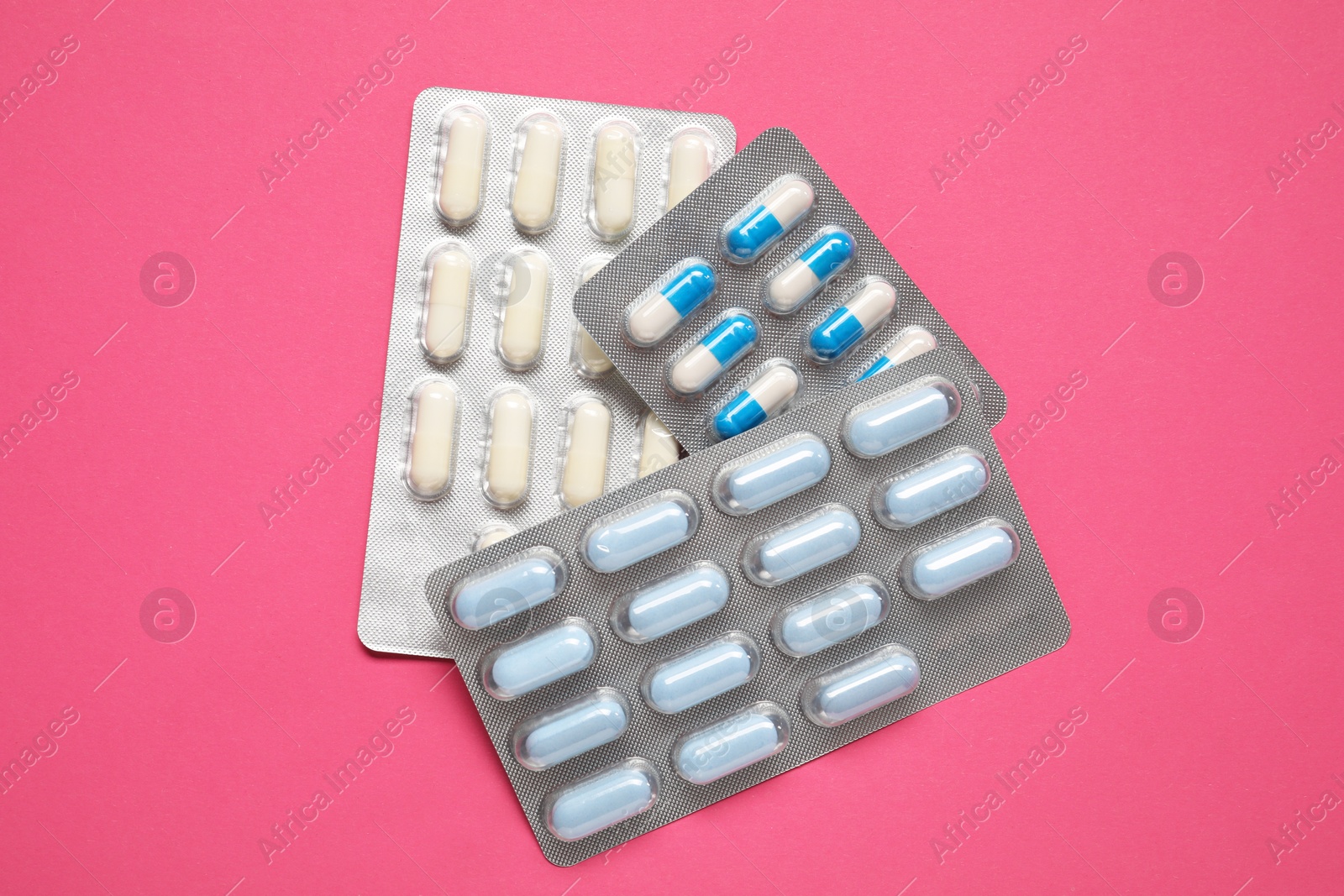 Photo of Different antibiotic pills in blisters on pink background, top view