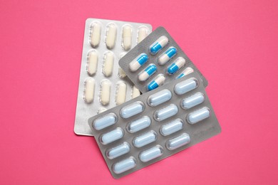 Photo of Different antibiotic pills in blisters on pink background, top view