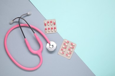 Antibiotic pills in blisters and stethoscope on color background, flat lay. Space for text