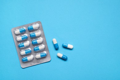 Photo of Antibiotic pills in blister on light blue background, top view. Space for text