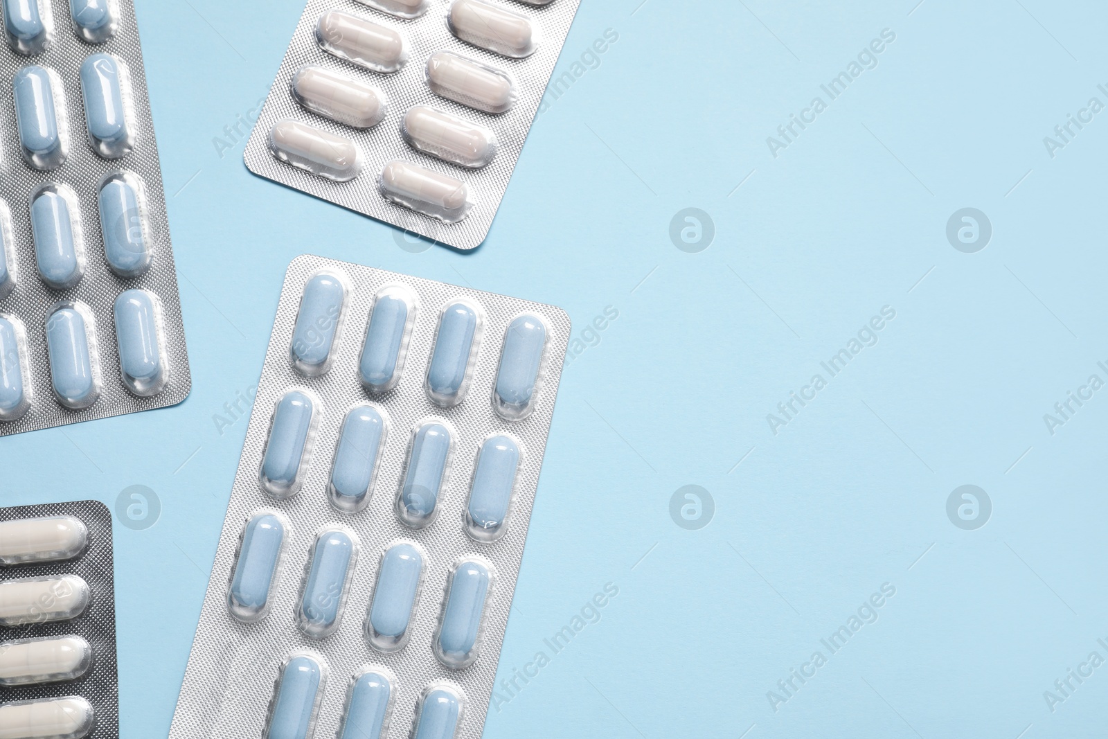 Photo of Different antibiotic pills in blisters on light blue background, flat lay. Space for text