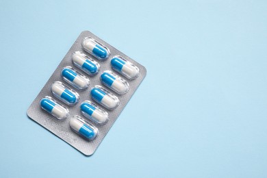 Photo of Antibiotic pills in blister on light blue background, top view. Space for text