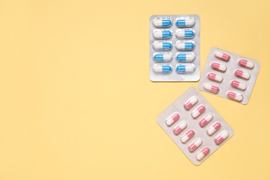 Different antibiotic pills in blisters on yellow background, flat lay. Space for text