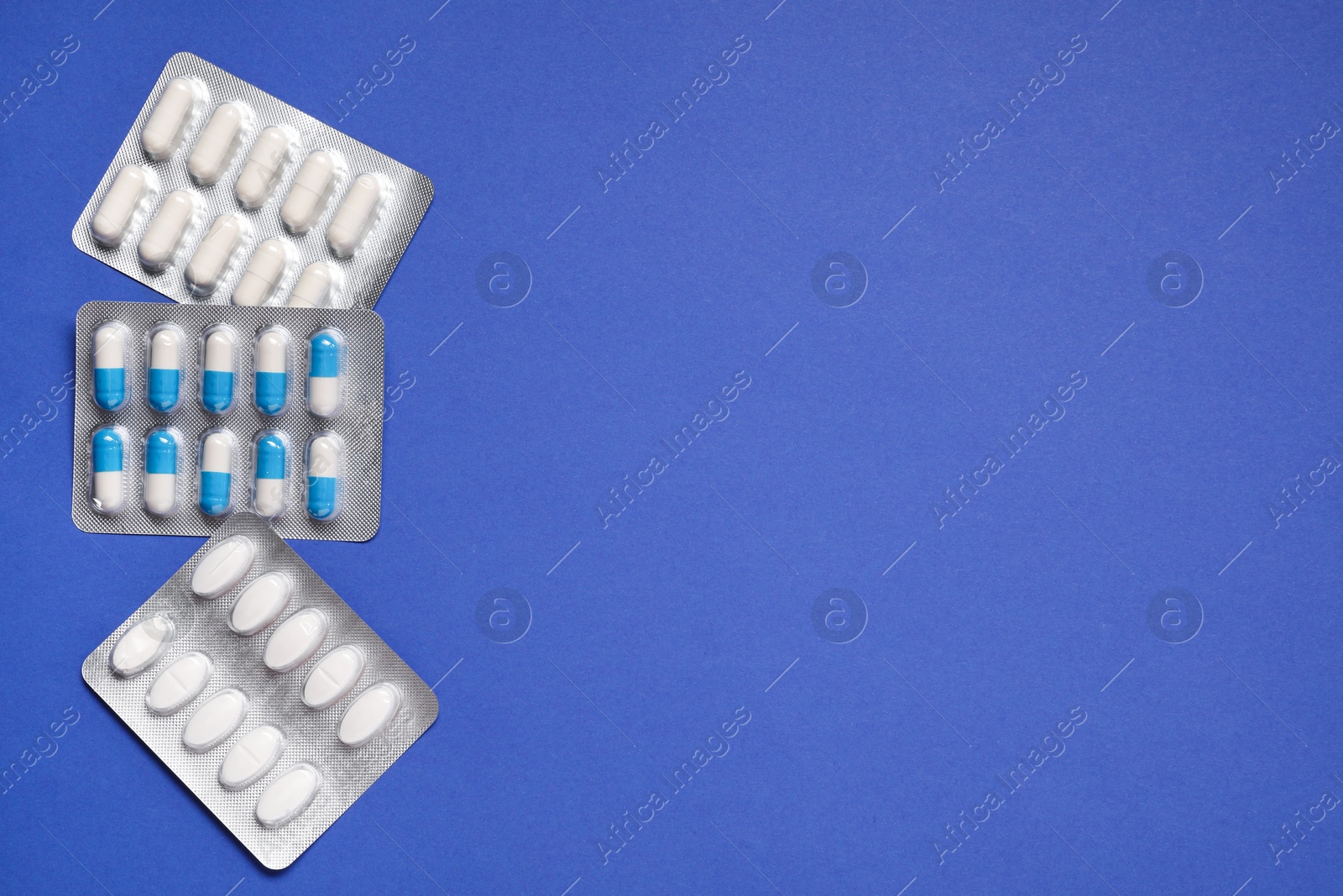 Photo of Different antibiotic pills in blisters on blue background, flat lay. Space for text