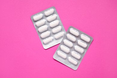 Antibiotic pills in blisters on pink background, top view