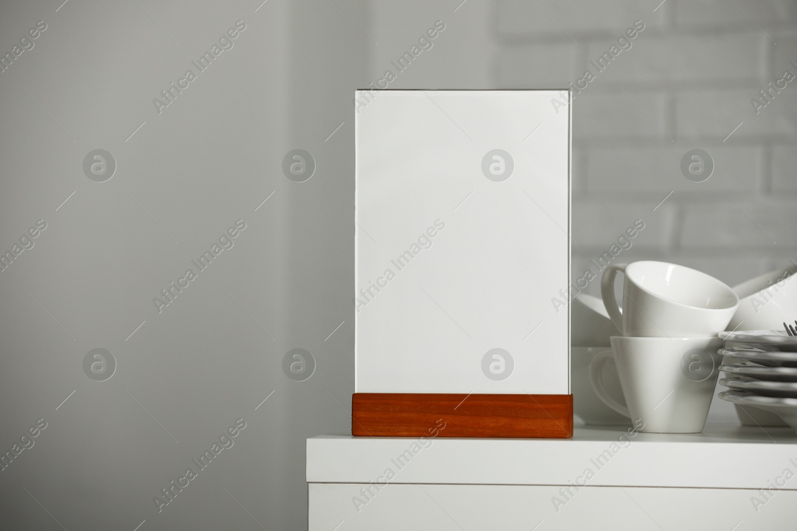 Photo of Menu holder and clean dishware on white table indoors, space for text