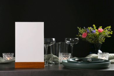 Photo of Menu holder, clean dishware and burning candles on grey table against black background