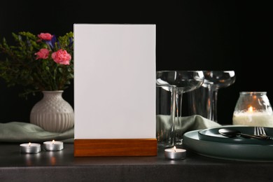 Photo of Menu holder, clean dishware and burning candles on grey table against black background