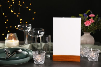 Photo of Menu holder, clean dishware and burning candles on grey table against blurred lights