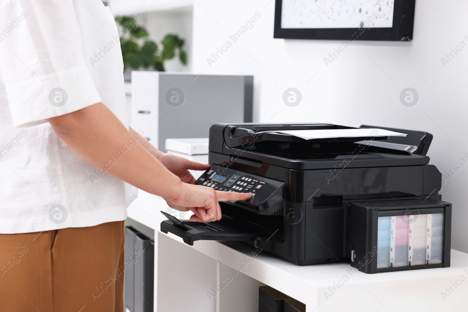 Photo of Woman using modern printer at workplace indoors, closeup