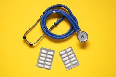 Photo of Antibiotic pills in blisters and stethoscope on yellow background, top view