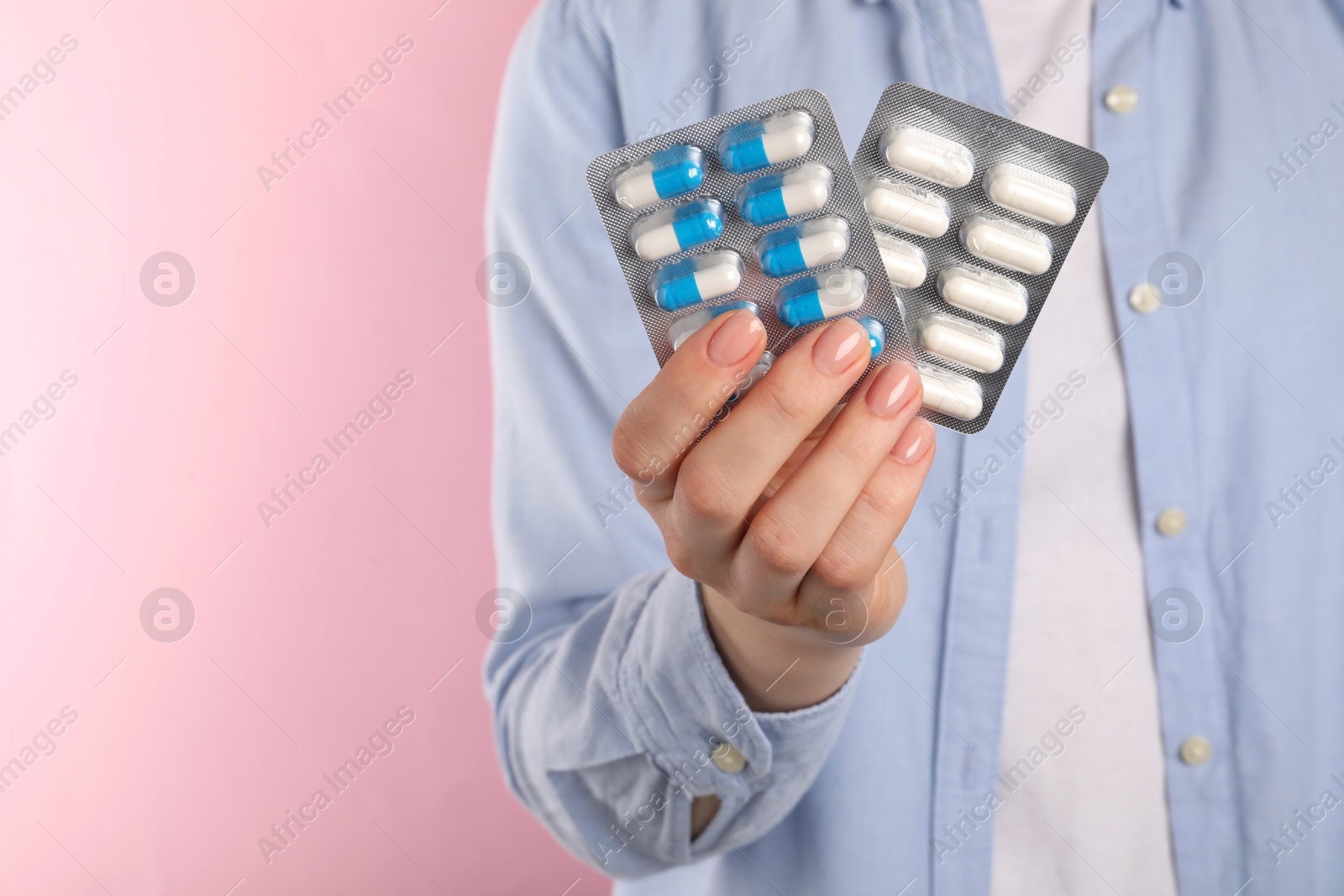 Photo of Woman holding blisters with antibiotic pills on pink background, closeup. Space for text