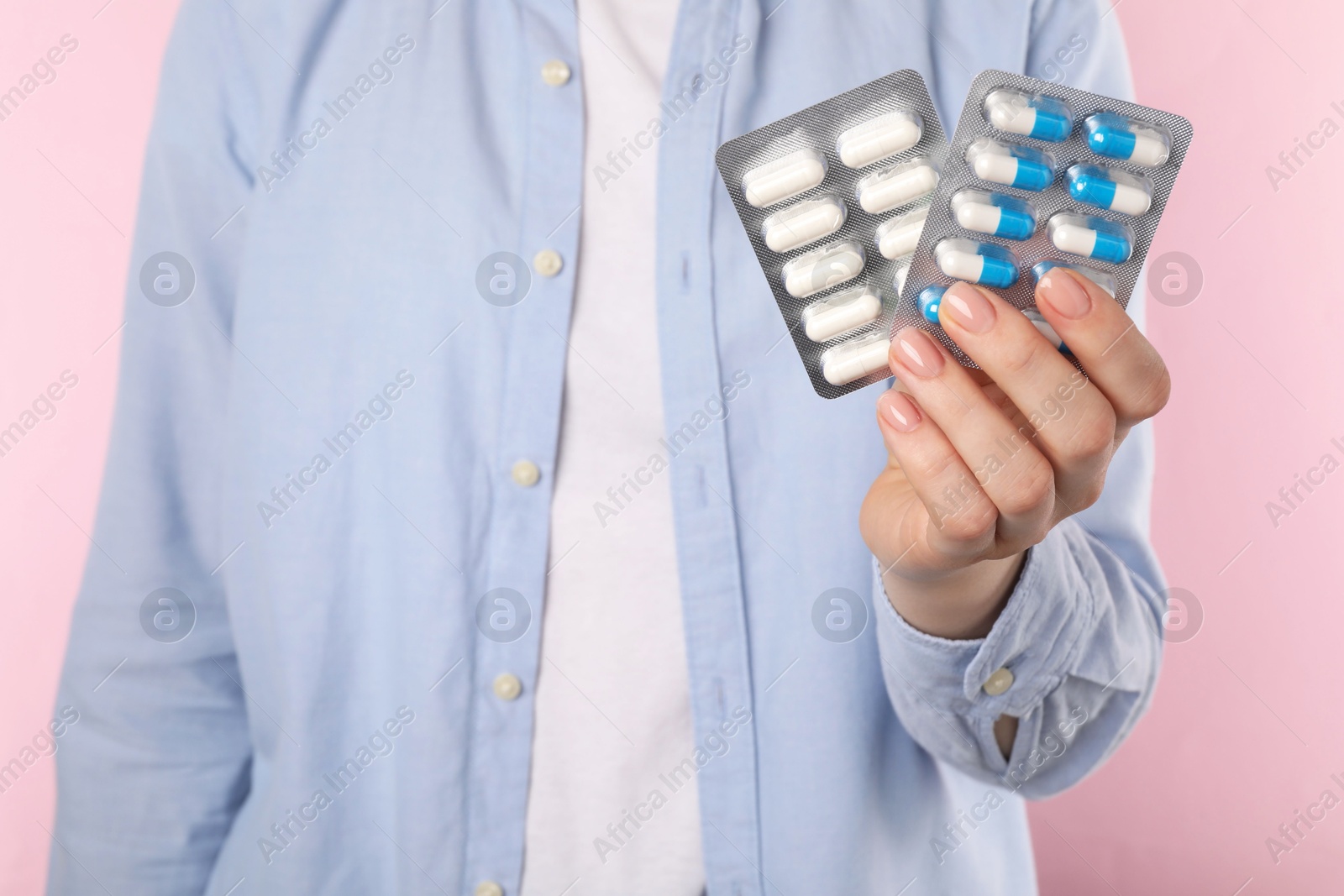 Photo of Woman holding blisters with antibiotic pills on pink background, closeup