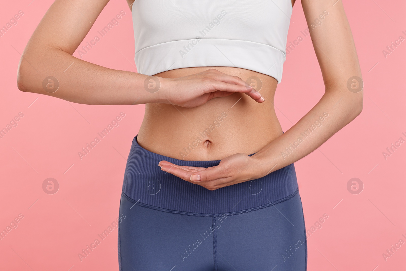 Photo of Healthy digestion. Woman holding something near her belly on pink background, closeup