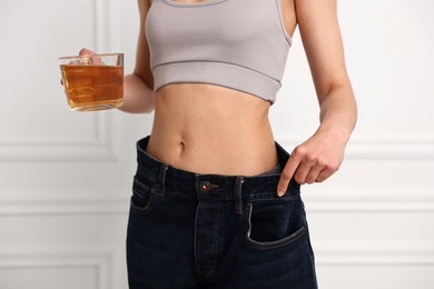 Weight loss concept. Woman with cup of diet tea and big pants near white wall, closeup