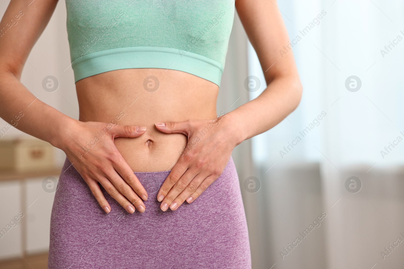 Photo of Healthy digestion. Woman making heart shape with hands near her belly indoors, closeup