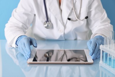 Doctor with tablet at table against light blue background, closeup view