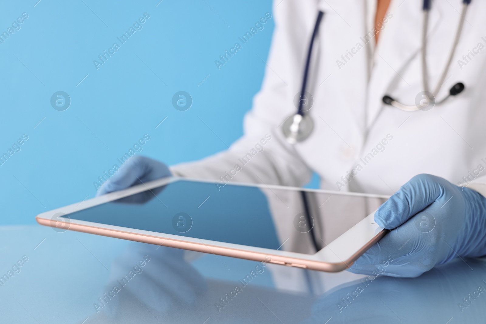 Photo of Doctor with tablet at table against light blue background, closeup view