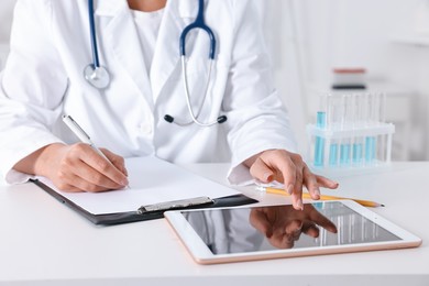 Doctor with tablet at table in clinic, closeup view