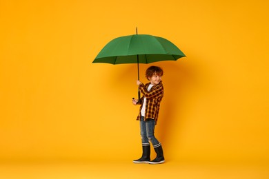 Little boy with green umbrella on orange background