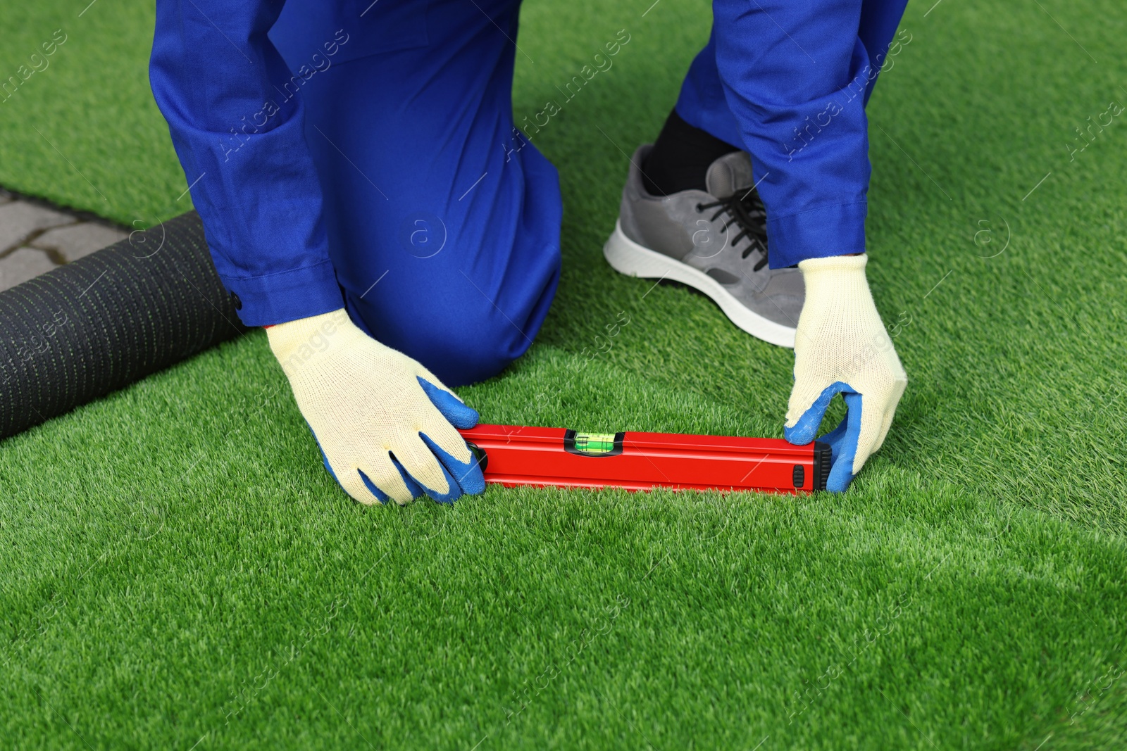 Photo of Man in uniform installing artificial turf outdoors, closeup