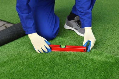 Photo of Man in uniform installing artificial turf outdoors, closeup