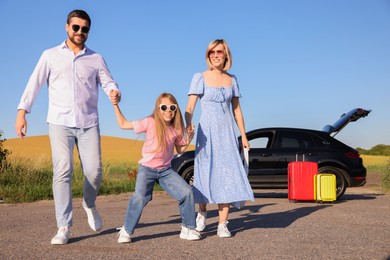 Parents, their daughter, car and suitcases outdoors. Family traveling