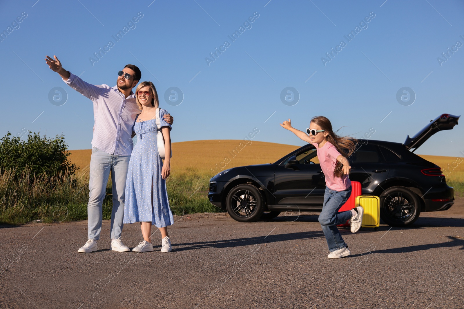 Photo of Parents, their daughter, car and suitcases outdoors. Family traveling