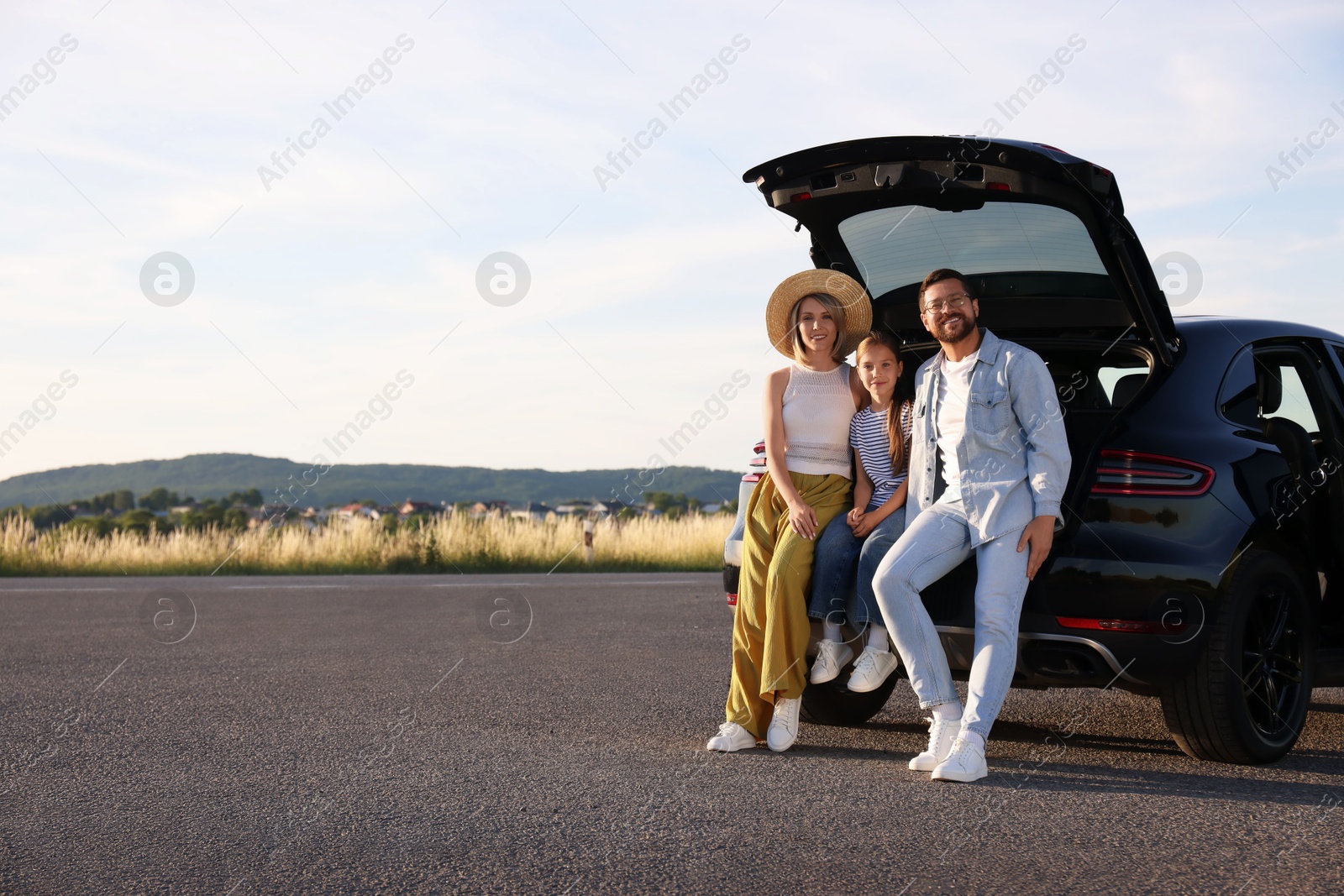 Photo of Happy family sitting in trunk of car outdoors, space for text