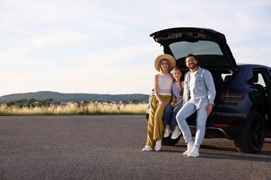 Happy family sitting in trunk of car outdoors, space for text