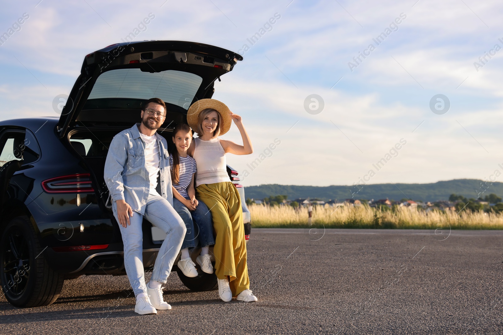 Photo of Happy family sitting in trunk of car outdoors, space for text