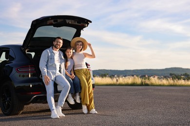 Photo of Happy family sitting in trunk of car outdoors, space for text