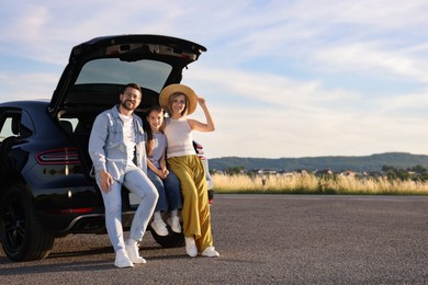 Happy family sitting in trunk of car outdoors, space for text