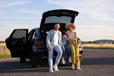 Photo of Happy family sitting in trunk of car outdoors