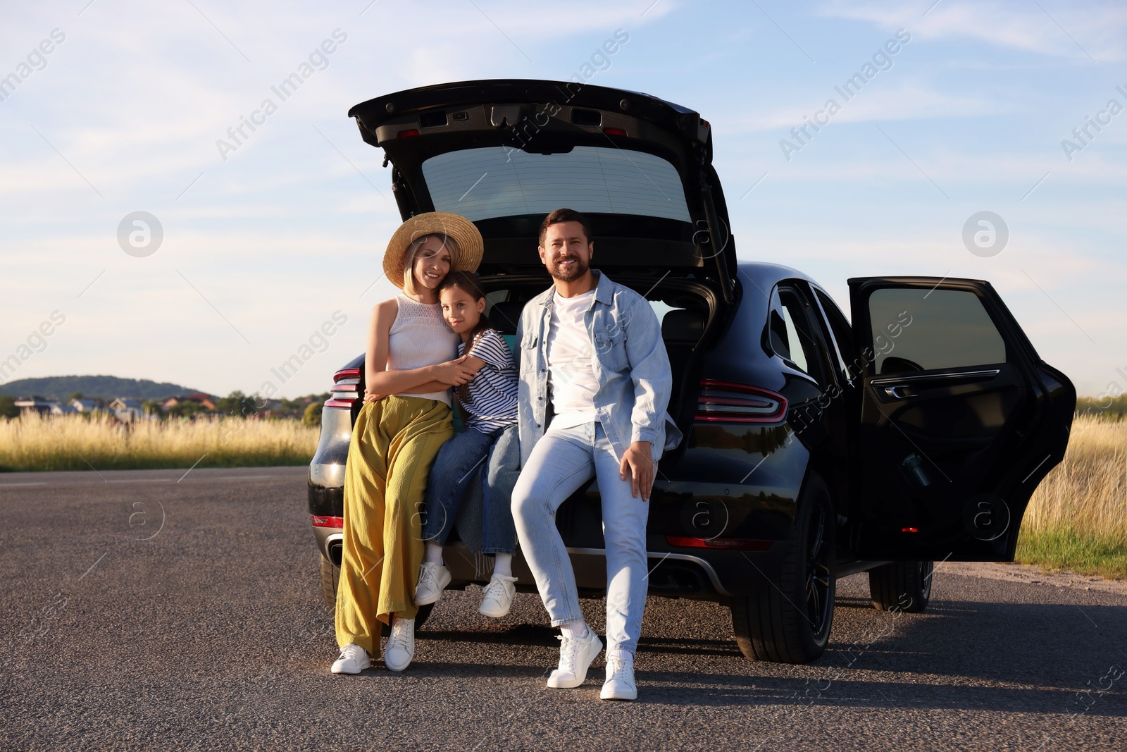 Photo of Happy family sitting in trunk of car outdoors