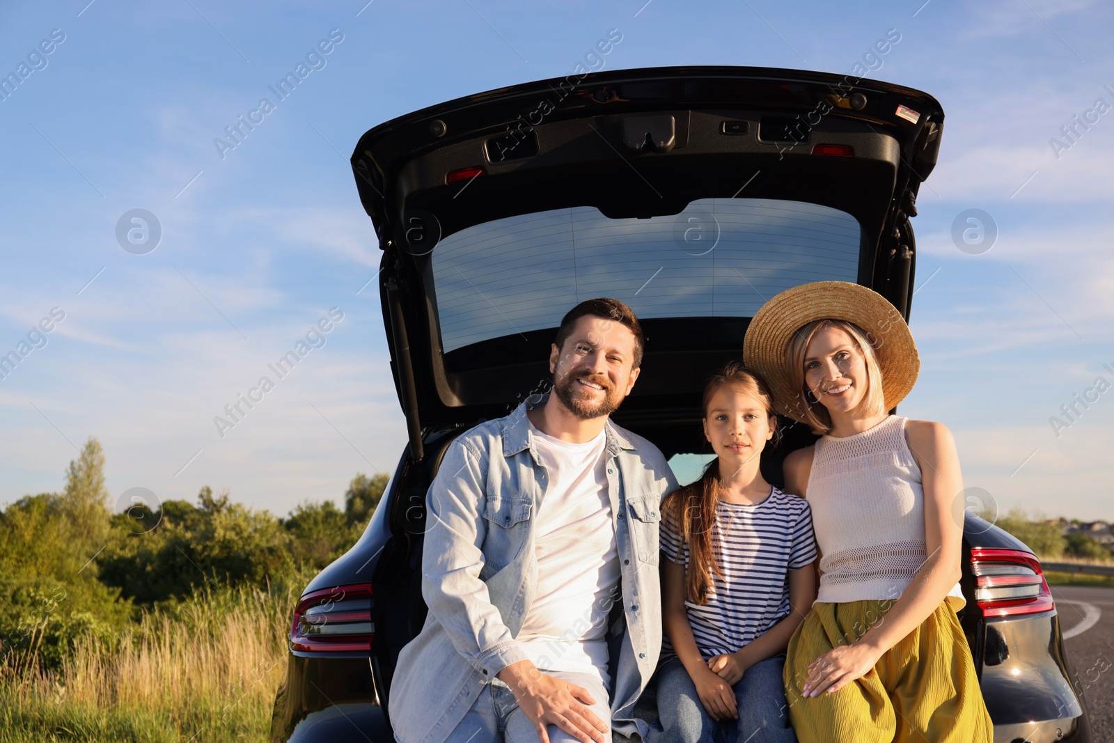 Photo of Happy family sitting in trunk of car outdoors