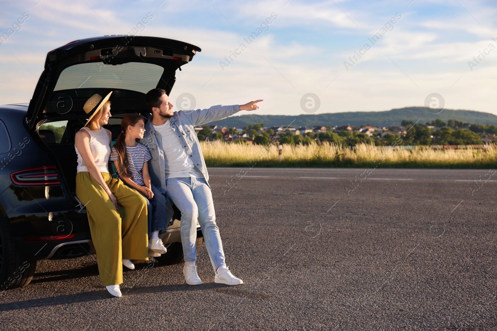 Photo of Happy family sitting in trunk of car outdoors, space for text