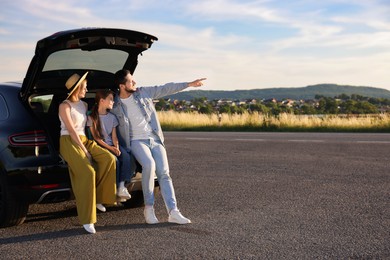 Happy family sitting in trunk of car outdoors, space for text