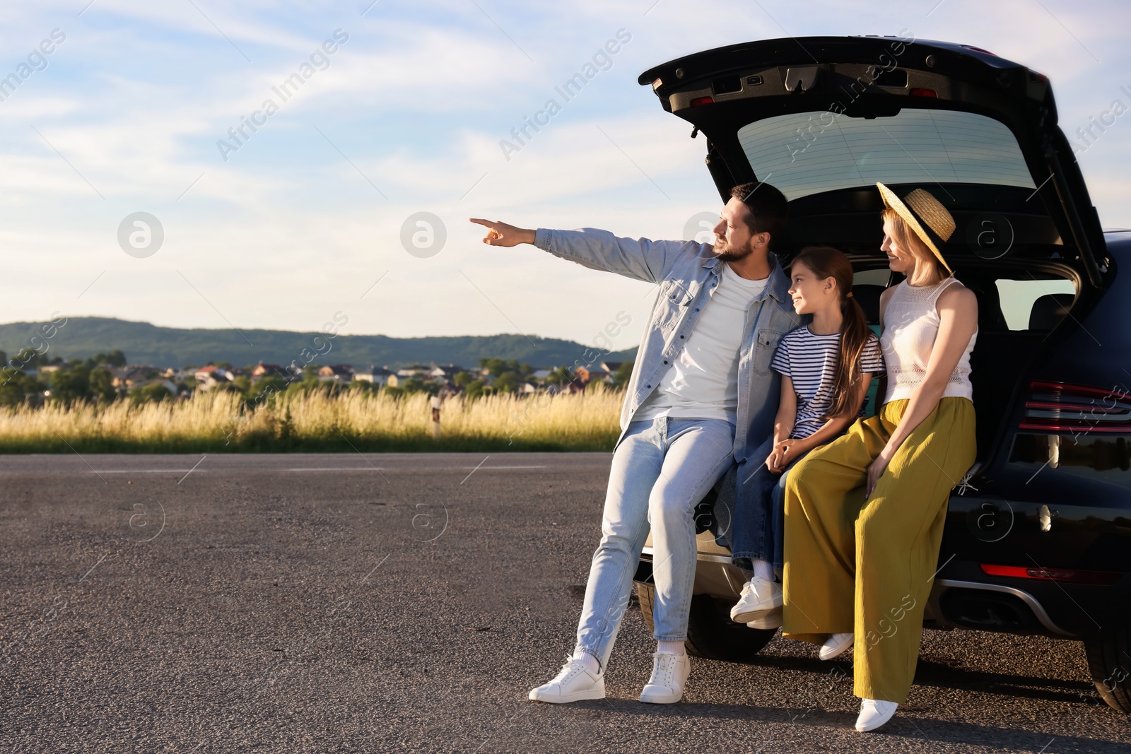 Photo of Happy family sitting in trunk of car outdoors, space for text