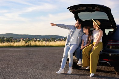 Happy family sitting in trunk of car outdoors, space for text