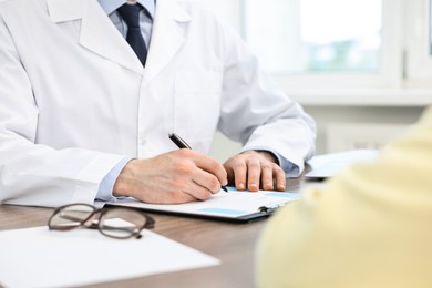 Photo of Doctor writing prescription for patient at wooden table in clinic, closeup