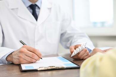 Photo of Doctor writing prescription for patient at wooden table in clinic, closeup