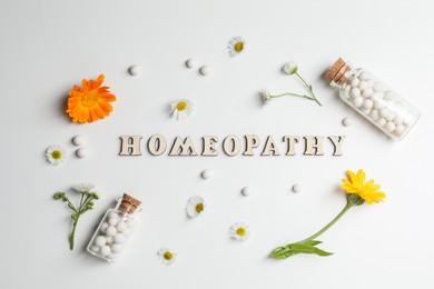 Photo of Word Homeopathy, pills and medicinal herbs on white background, flat lay